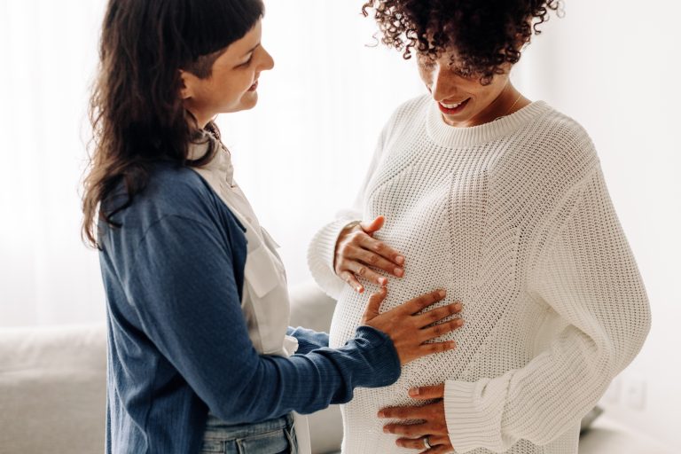 LGBTQ couple touching the belly of a female-presenting person with a pregnant belly.