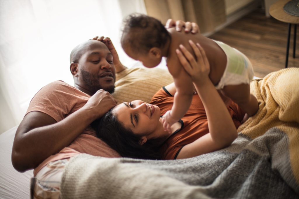 Two parents on bed holding their baby