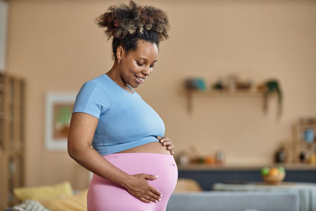 Pregnant Black woman at home holding her belly.