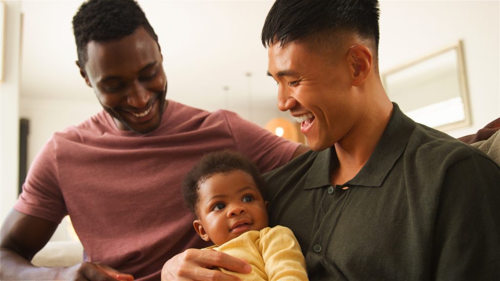 Fathers share laughter and joy while holding their baby in a warm setting.