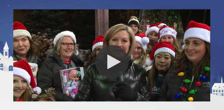 Reporter talking to the microphone. They are surrounded by patient families all wearing red Santa hats